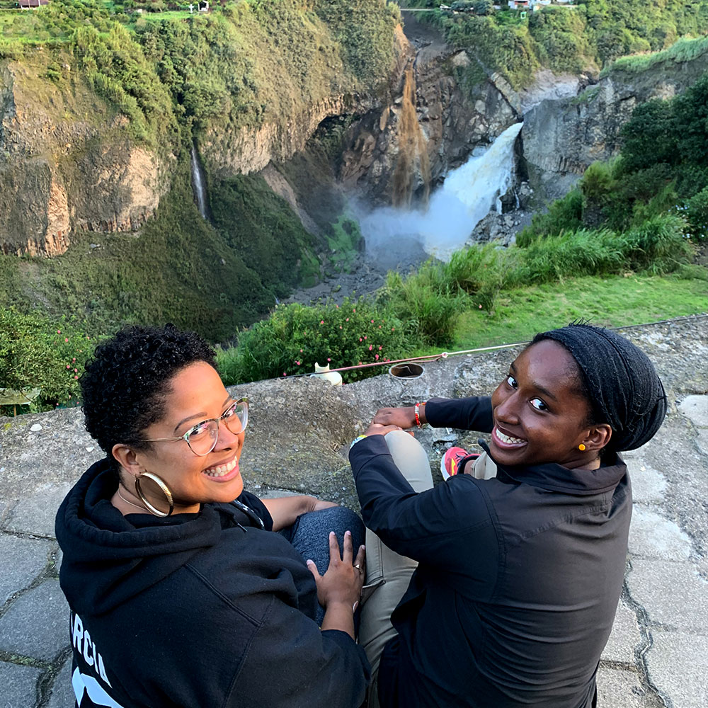 two joy-filled women sitting on top of a cliff with a misty river stream visible below